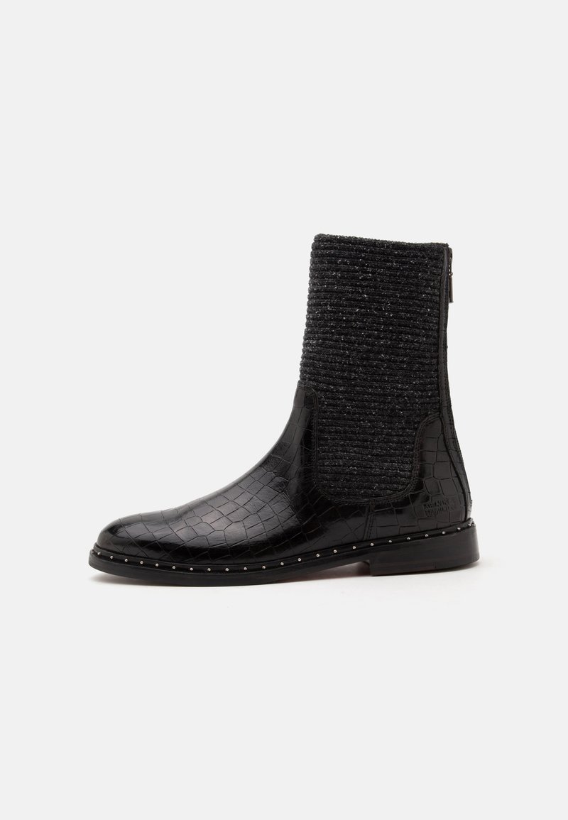 Botte noire mi-mollet avec texture crocodile brillante, dessus en tissu tricoté, fermeture éclair latérale et petits clous métalliques le long du bord de la semelle.