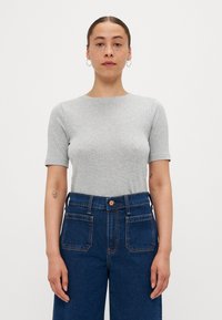 Šedé tričko s krátkým rukávem vyrobené z hladké, lehké tkaniny, spárované s džíny z tmavě modrého denimu s vysokým pasem, které mají kapsy a knoflík.