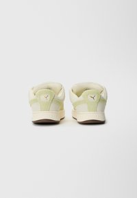 Ein Paar beiger und hellgrüner Puma Sneaker im Low-Top-Stil von hinten auf einem schlichten weißen Hintergrund betrachtet.