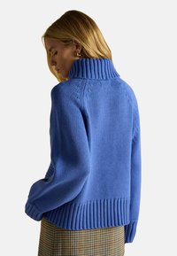 Gruby niebieski sweter dzianinowy z wysokim prążkowanym kołnierzem i prążkowanym wykończeniem. Posiada detale w sploty kablowe na ramionach. Miękka, teksturowana tkanina.