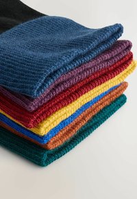 Stak af strikkede uldsokker i sort, navy, lilla, rød, gul, blå, brun og grøn farve på en hvid overflade.