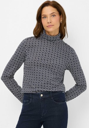 Maglione a collo alto blu navy in tessuto elastico con un motivo geometrico bianco. Maniche lunghe e silhouette aderente. Abbinato a jeans scuri.
