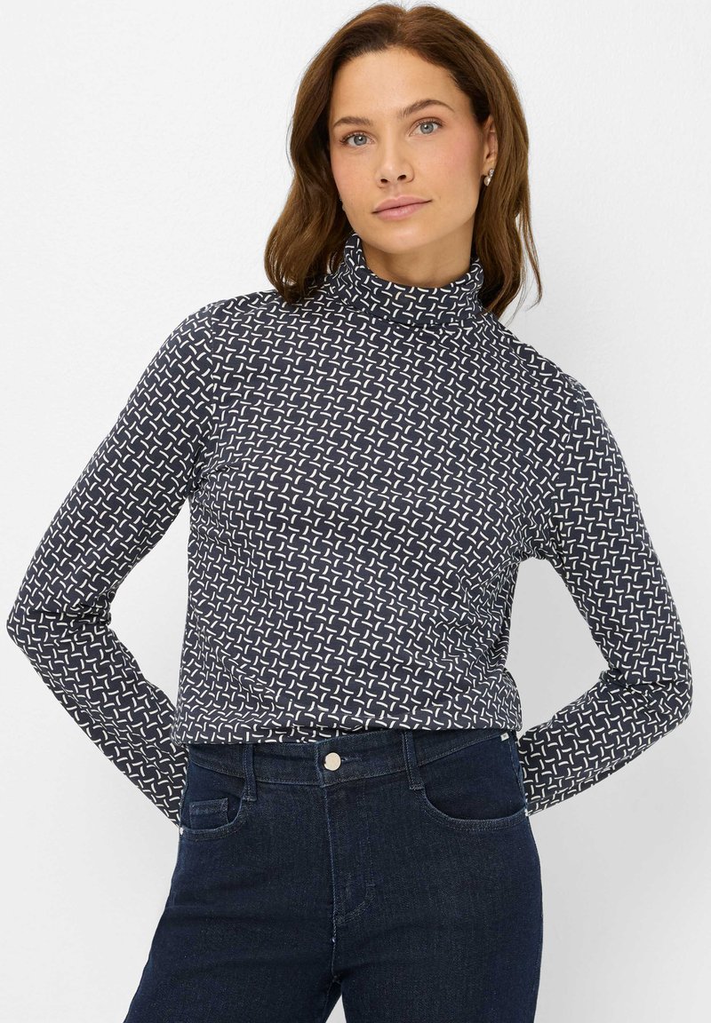 Maglione a collo alto blu navy in tessuto elastico con un motivo geometrico bianco. Maniche lunghe e silhouette aderente. Abbinato a jeans scuri.