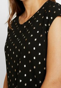 Top nero con scollo a giro e maniche corte, con motivo a pois metallici argento e oro su tutta la superficie del tessuto. Texture morbida.