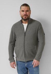 Grauer Zip-Up-Cardigan aus weichem Stoff, mit hohem Kragen, gerippten Bündchen und seitlichen Taschen. Trägt man über einem weißen T-Shirt.