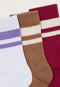 Pruhované ponožky v troch farbách: biele s fialovými pruhmi, hnedé s krémovými pruhmi a červené s krémovými pruhmi; rebrovaná textúra.