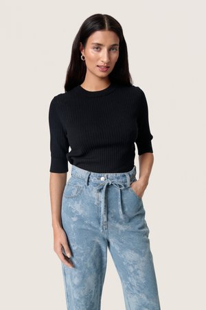 Top corto a maniche corte nero a coste abbinato a jeans in denim azzurri chiari a vita alta con dettaglio annodato davanti e leggera sfumatura.