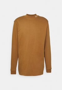 Svetr s dlouhými rukávy, vysokým límcem a hořčicově hnědou barvou, vyrobený z měkké bavlny, s malým bílým logem na límci a žebrovanými manžetami.