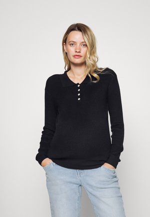 Suéter de malha canelada preto com colarinho, apresentando uma linha de botões e mangas compridas. Combinado com jeans de um tom azul claro.