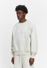 Hellgrauer Sweatshirt aus weichem Material mit Rundhalsausschnitt und gerippten Bündchen. Mit einem verblassten Druck auf der Vorderseite und lockerer Passform.