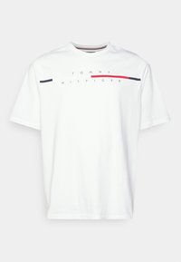 Camiseta de algodón blanca con cuello redondo, mangas cortas y texto impreso "TOMMY HILFIGER" con líneas horizontales rojas y azul marino en el pecho.