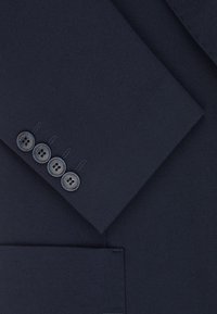 Granatowy materiał garniturowy o strukturalnym splocie. Posiada dopasowany klapę i cztery szare guziki z subtelnym detalem logo na mankietach.