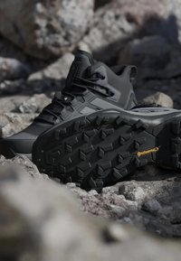 Chaussure de randonnée noire avec semelle en caoutchouc texturé, présentant un design épuré, un embout renforcé et des lacets ajustables pour un maintien sûr.