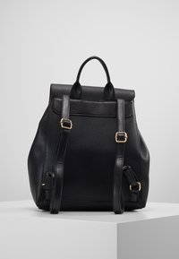 Mochila de cuero negro con un acabado texturizado, que cuenta con herrajes dorados, dos correas ajustables y una solapa superior con un asa.