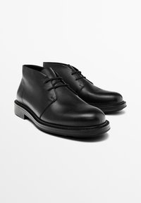 Bottines en cuir noir avec une texture lisse, bout rond et détail de lacets. Caractéristiques d'une semelle basse et durable et d'un design simple.