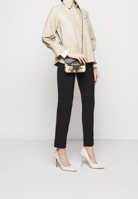 Beige värinen rakenteinen paita, mustat istuvat housut, valkoiset korkokengät ja pieni käärmekuvioitu käsilaukku, jossa on musta hihna.