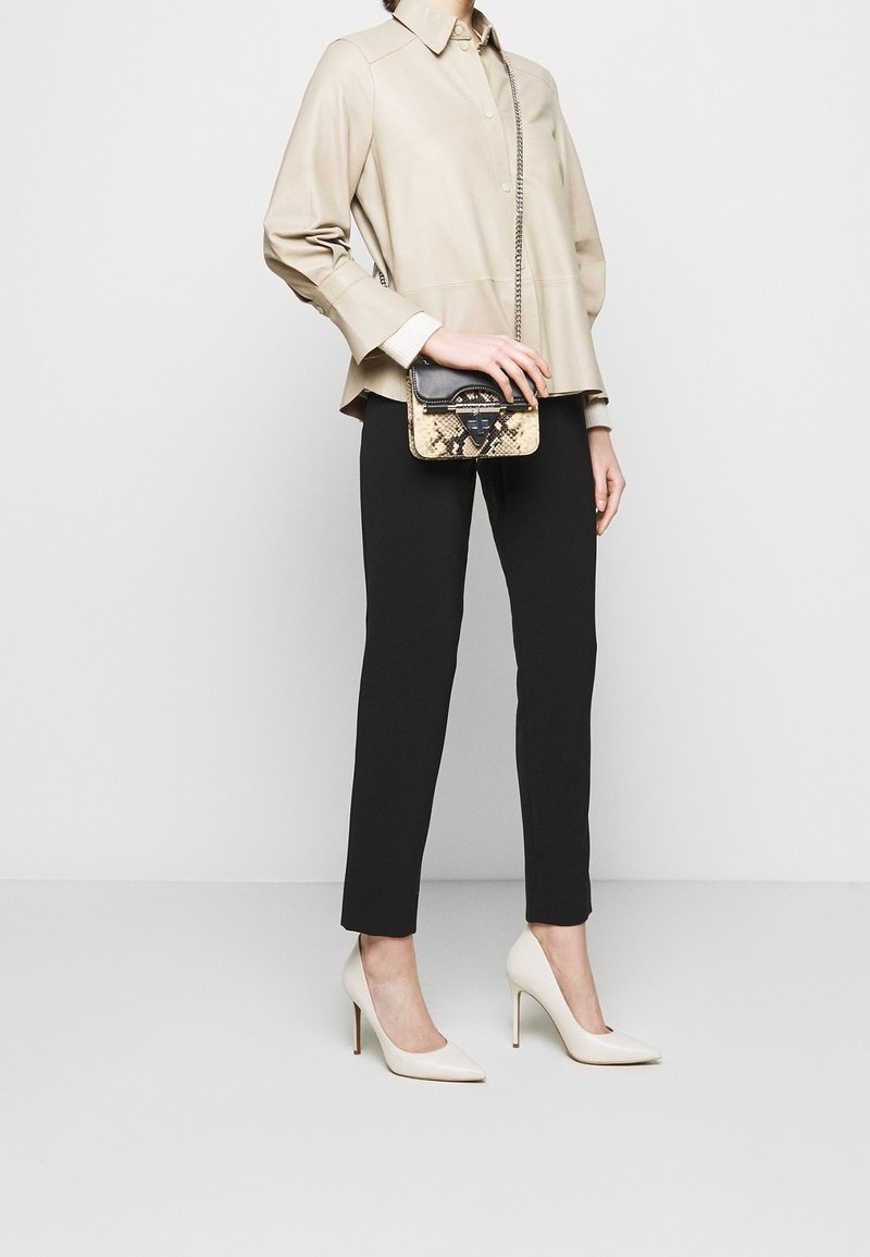 Beige värinen rakenteinen paita, mustat istuvat housut, valkoiset korkokengät ja pieni käärmekuvioitu käsilaukku, jossa on musta hihna.