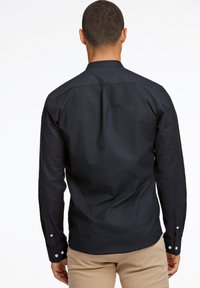 Cămașă albastră închis cu mânecă lungă, cu spate ajustat, manșete cu butoni și textură subtilă. Design croițat, tiv curbat și guler clasic.