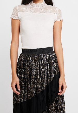 Hvid top med blonde korte ærmer og høj hals, parret med en sort plisseret nederdel med guld- og sølvmetallic detaljer.