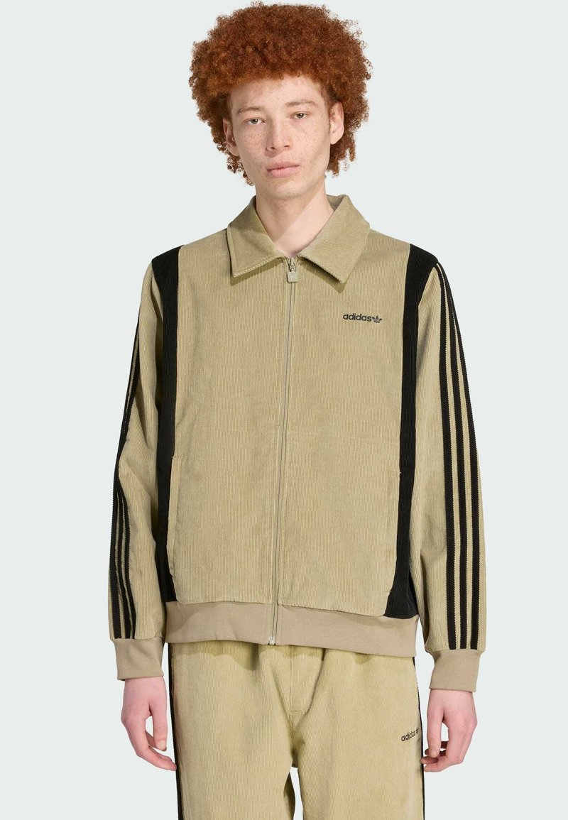 Beige corduroy jacket with black side stripes and zip closure. Features a collared neck and embroidered branding on the chest.