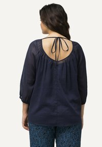 Blusa blu navy realizzata in tessuto leggero, con schiena scooped e lacci, maniche a 3/4 e design sfuso.