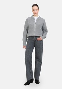 Sudadera gris con cremallera y textura acanalada, combinada con unos vaqueros oscuros de cintura alta y corte holgado. Unos zapatos negros completan el conjunto.