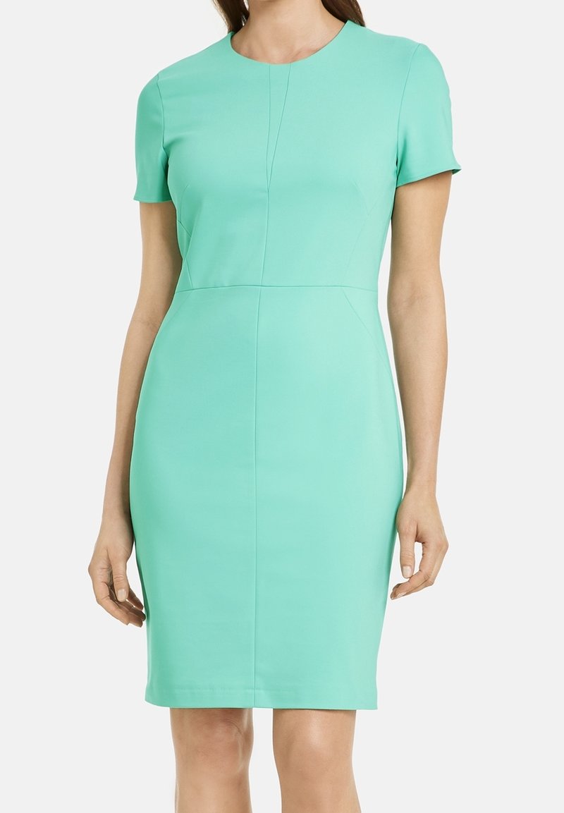 Femme portant une robe ajustée, longueur genou, manches courtes, turquoise clair uni avec un col rond et des détails subtils de coutures.