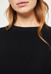 Schwarzer, gerippter Strickpullover mit rundem Ausschnitt. Die Textur ist leicht erhaben und zeigt ein eng anliegendes Design.