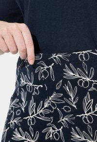 Tessuto blu navy con motivo di rami d'olivo bianchi, dotato di una tasca. Il design presenta una texture liscia e una silhouette aderente.