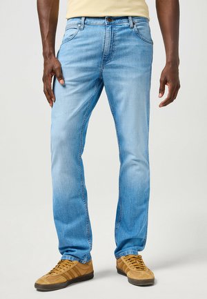 Jeans in denim azzurro chiaro con taglio dritto, design a cinque tasche, leggera sbiaditura e un bottone marrone in vita. Abbinati a sneakers color cammello.