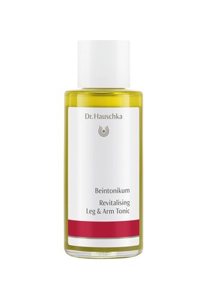 Clear glass bottle with a white cap, filled with yellow liquid. Label displays "Dr. Hauschka Beintonikum Revitalising Leg & Arm Tonic" with red accents.