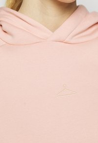 Rosa hoodie med en mjuk textur och en subtil hängare-logotyp broderad i ljus färg på bröstet. Cowl-halsringning med en avslappnad passform.