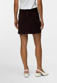 Gonna in corduroy marrone con taglio dritto, lunghezza a metà coscia e zip sul retro. Abbinata a décolleté bianche con tacco chunky.