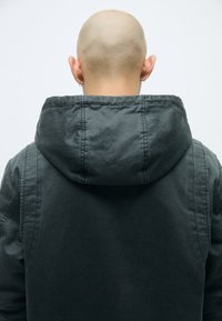 Σκοτεινός γκρι φούτερ jacket με απλή υφή, εμφανή ραφές στην κουκούλα και άνετη εφαρμογή, επανεξεταζόμενο από πίσω.