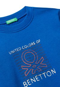 Niebieski sweter z prążkowanym kołnierzem, na którym znajduje się logo "United Colors of Benetton" oraz powtórzona nazwa marki w czarnym i białym kolorze.