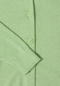 Manche d'un cardigan tricoté vert clair chevauchant le torse avec trois boutons ronds assortis alignés au centre devant.