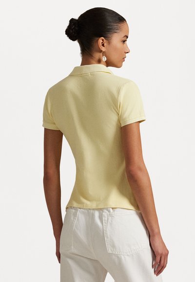 Dzeltena kokvilnas polo krekls ar klasisku apkakli un īsām piedurknēm; apvienots ar baltām biksēm, kas izceļ pieguļošu siluetu.