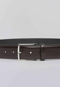 Brązowy pasek ze skóry o gładkim wykończeniu, z metalową srebrną sprzączką i pięcioma otworami do regulacji. Obszycie wzdłuż krawędzi.