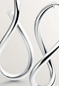 Pendientes de aro de plata con un diseño retorcido, textura suave y superficie brillante, que exhiben una forma fluida y contemporánea.
