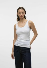 Débardeur blanc avec un décolleté plongeant et des bretelles étroites, en tissu lisse, associé à un jean en denim foncé.