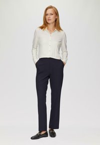 White long-sleeve button-up shirt with a collar paired with dark navy tailored trousers and black loafers. Simple design, smooth texture.
