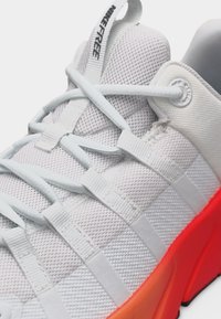 Λευκό αθλητικό παπούτσι Nike Free από διάτρητο υλικό με λευκά κορδόνια και πορτοκαλί σόλα, που δείχνει λεπτομέρειες στο πάνω μέρος και το λουράκι με το κείμενο της μάρκας.