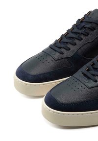 Navy sneakers crafted from textured leather and suede, featuring perforated detailing and a rubber sole with a beige accent.