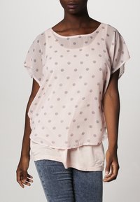 Blusa sheer rosa claro con sutiles lunares grises, cuello redondo, mangas cortas, diseño en capas y textura suave.