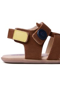Sandale marron pour tout-petit avec bride Velcro jaune et détail de bouton circulaire noir sur bride de cheville ajustable, semelle plate.