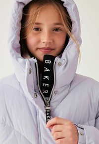 Világos levendula színű puffertakaró kapucnival, cipzáros záródással, fekete felirattal "BAKER" és steppelt mintázattal. Ezüst gombok láthatók.