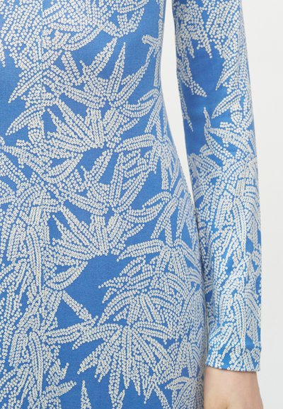 Κοντινό πλάνο μπλε υφάσματος με λευκό πουά λουλουδένιο σχέδιο και μακρύ μανίκι σε χέρι ατόμου.