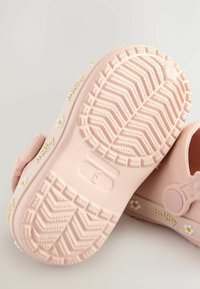Lyserøde gummisko med en struktureret sål. Har tusindfryd og "miffy" branding på siderne. Rundet design med en cirkulær knapdetalje.