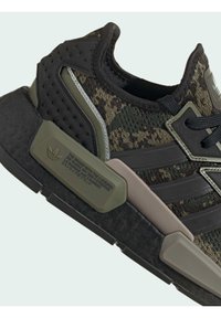 Sort og grøn camouflagemønstret Adidas-sneaker med sort sål, tyk polstring og mærket plastdetalje i neutrale farver.