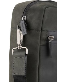 Bolso de cuero negro con textura mate, cierre con cremallera y herrajes metálicos. Incluye una correa cruzada con un accesorio de clip.